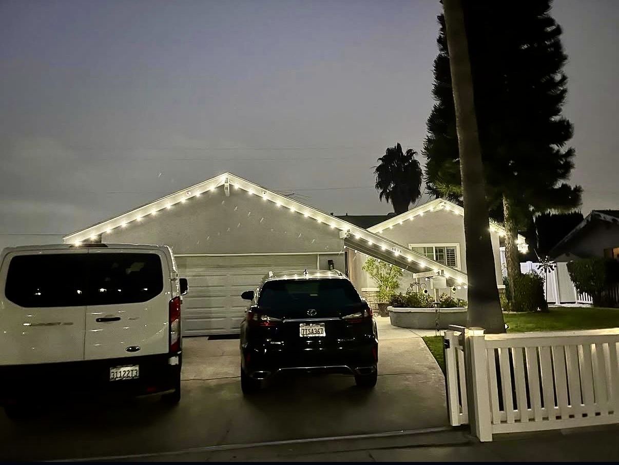 Ranch home with warm white roofline Christmas lighting at dusk, driveway view