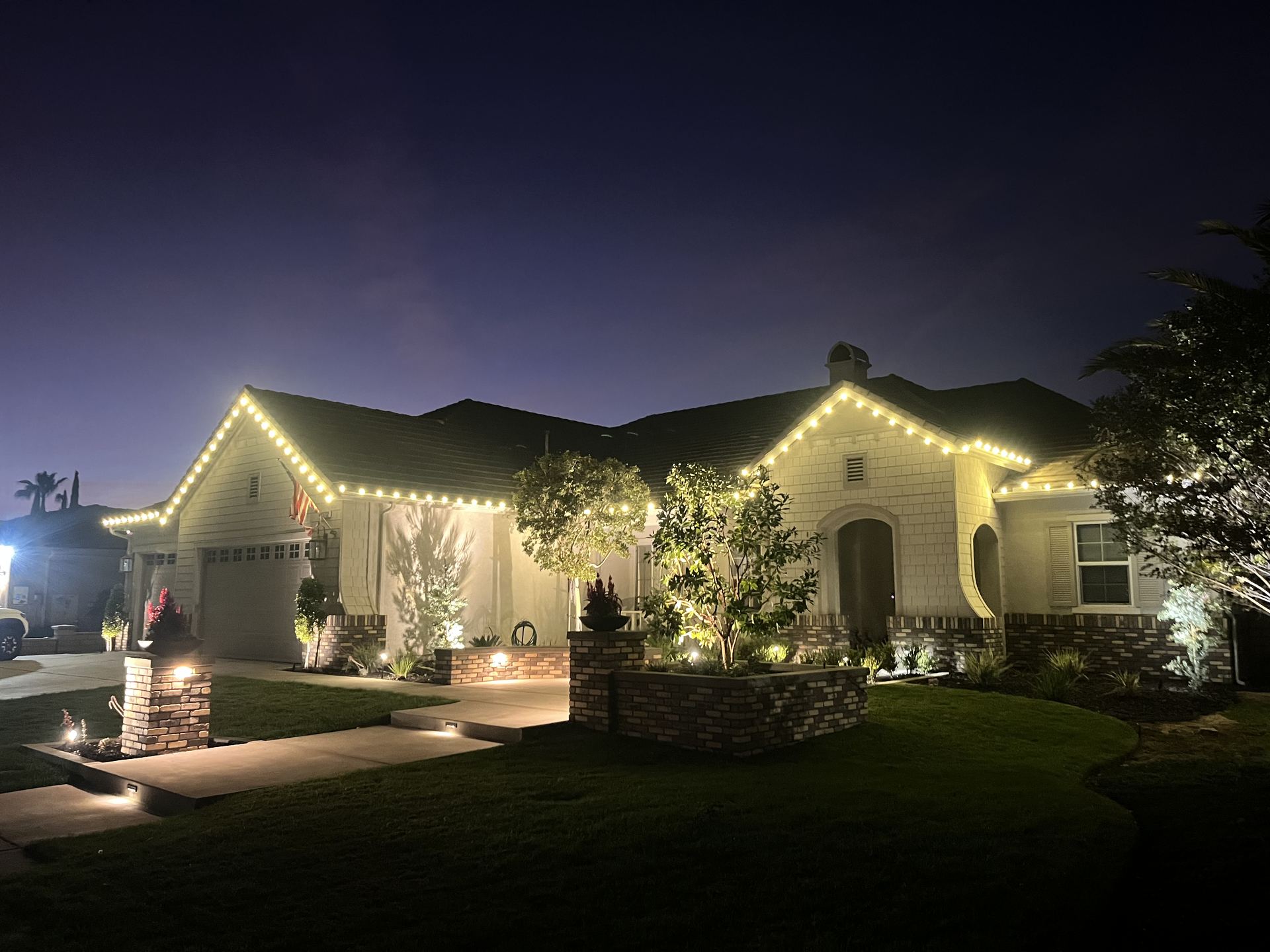 Single-story home with warm white roofline lighting and lit tree