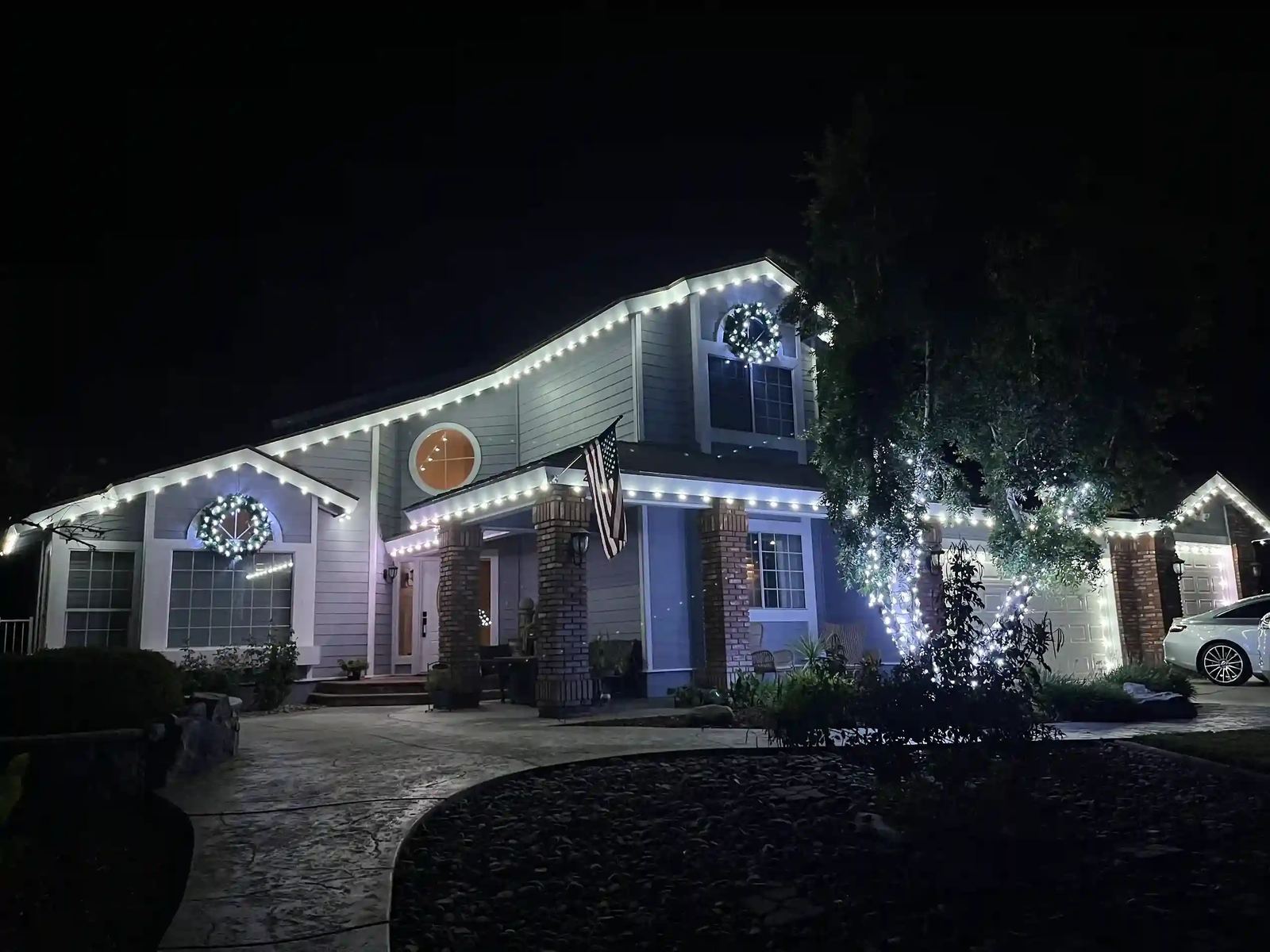 Christmas roofline lighting with wreaths on two-story farmhouse