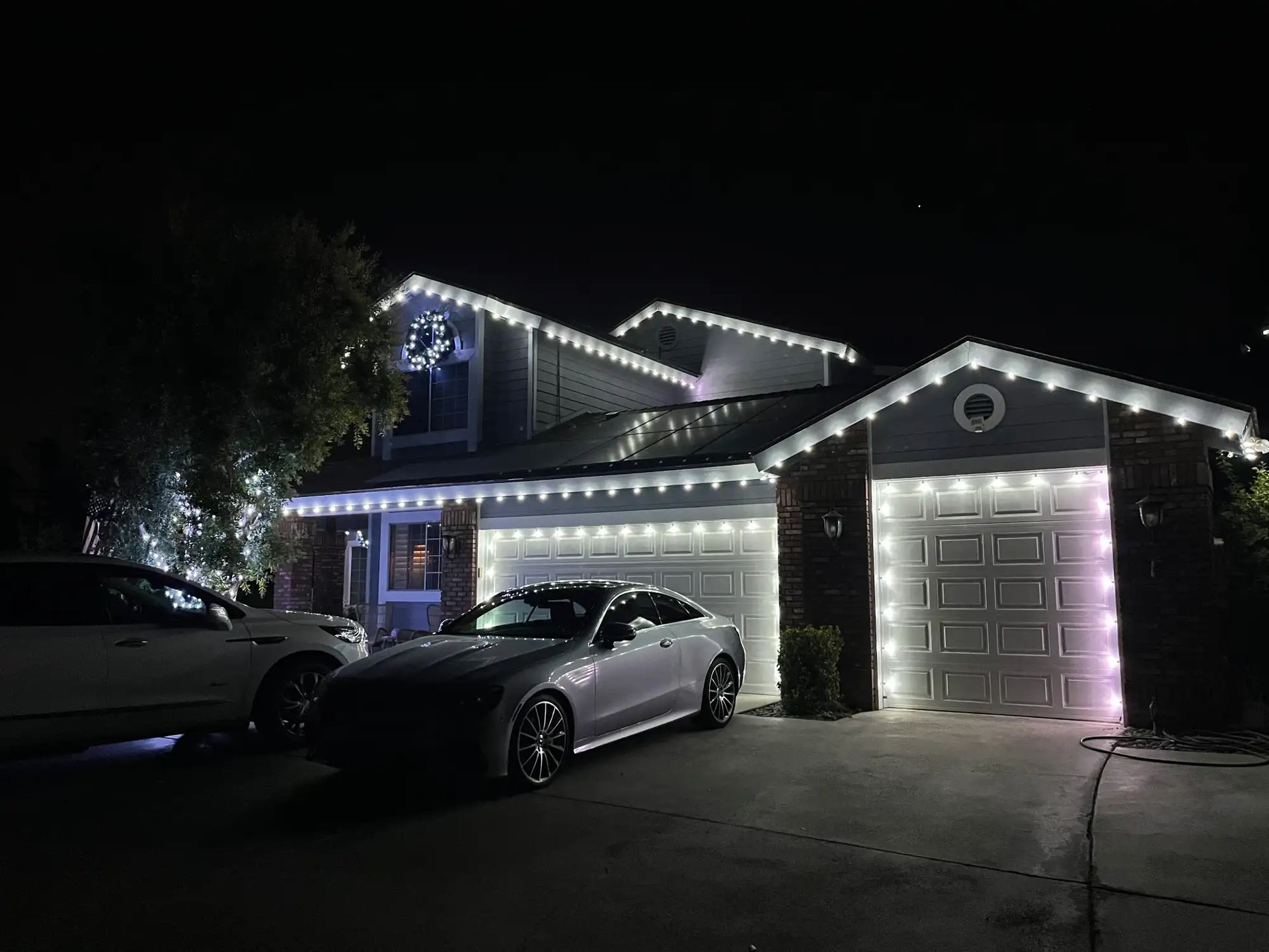 Two-story home with cool white roofline and garage door Christmas lighting