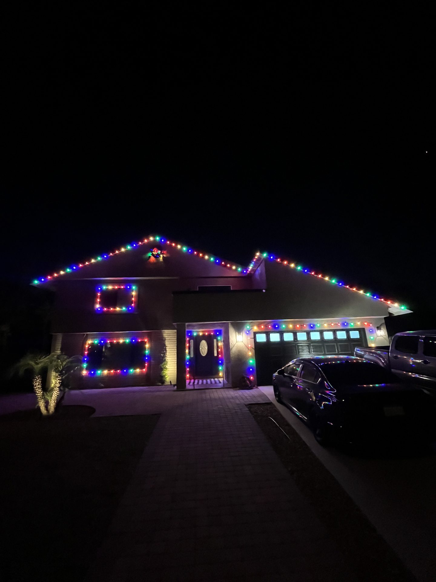 Two-story home with multicolor Christmas lighting over garage and driveway