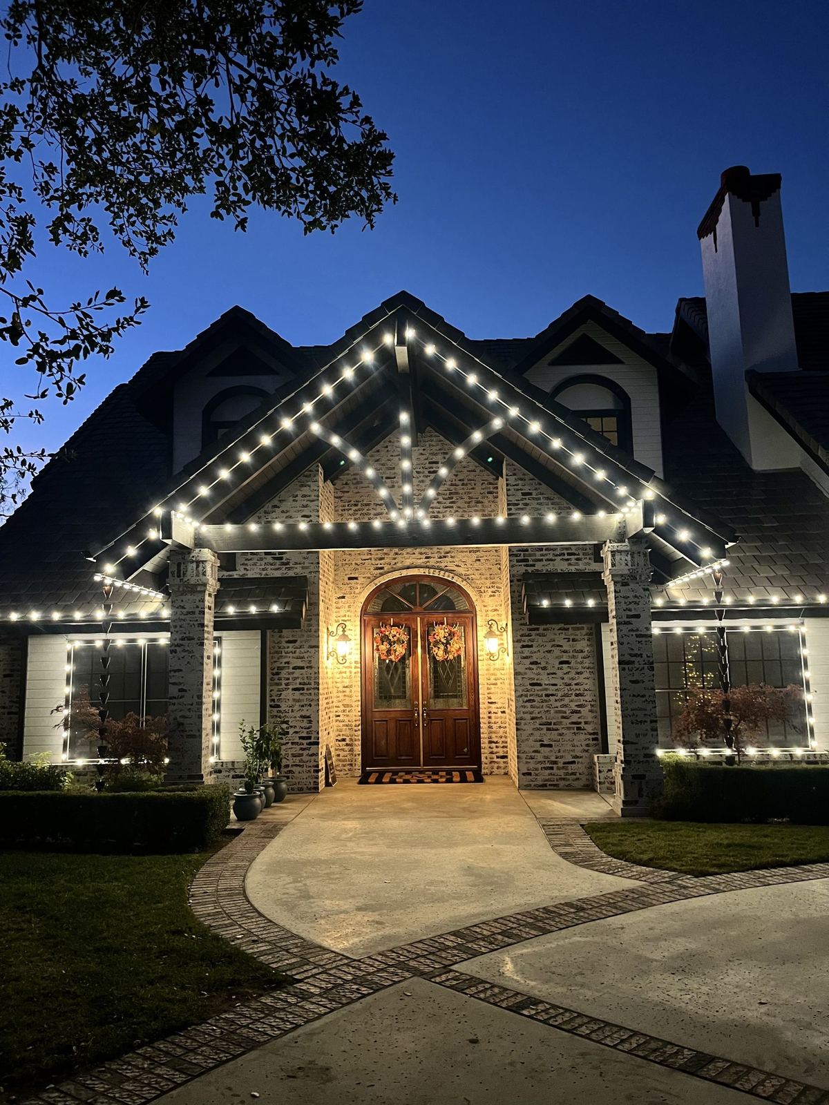 Warm white gable roofline lighting on white brick estate entryway