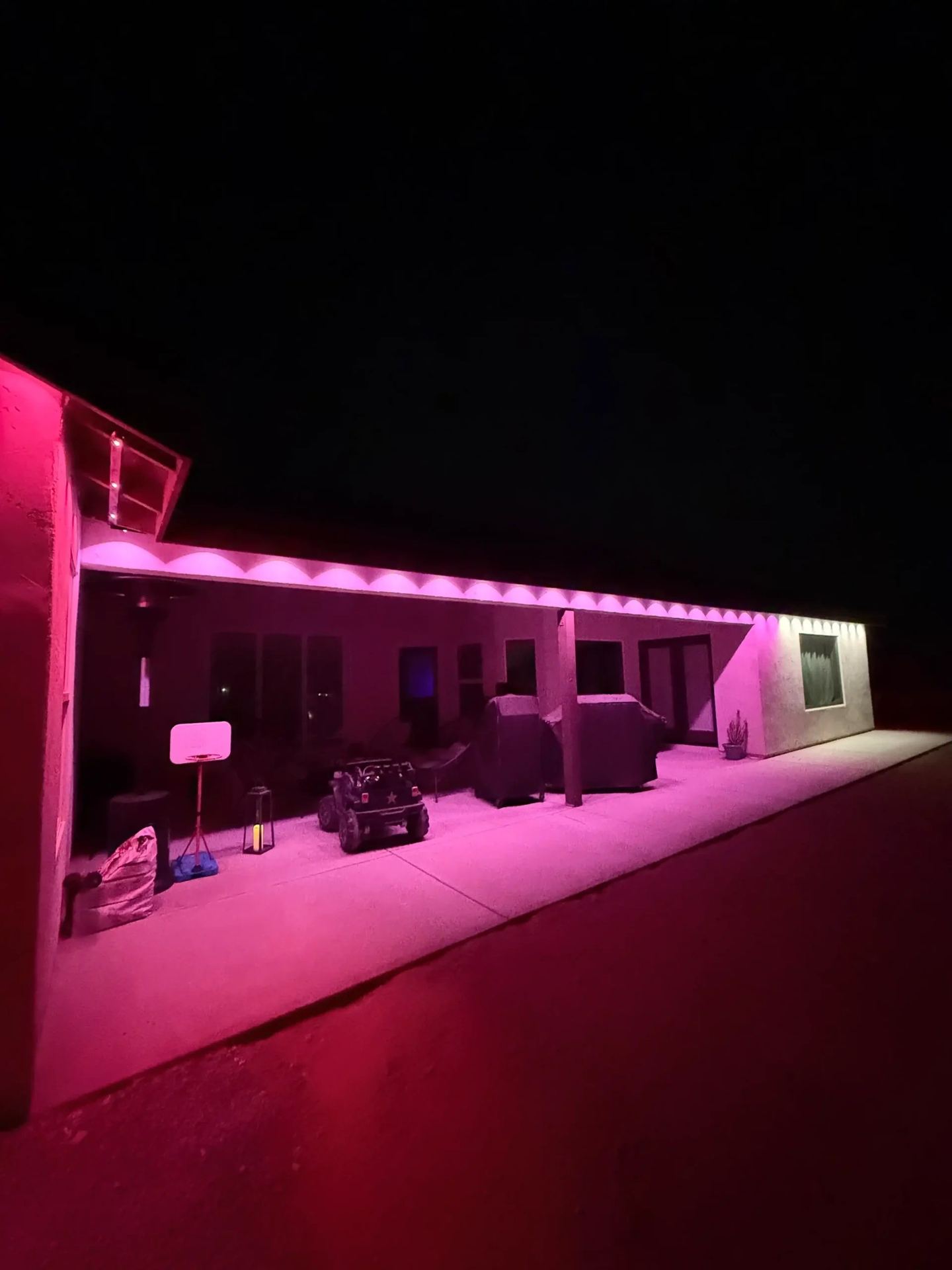Single-story home with pink and purple permanent lighting under carport at night