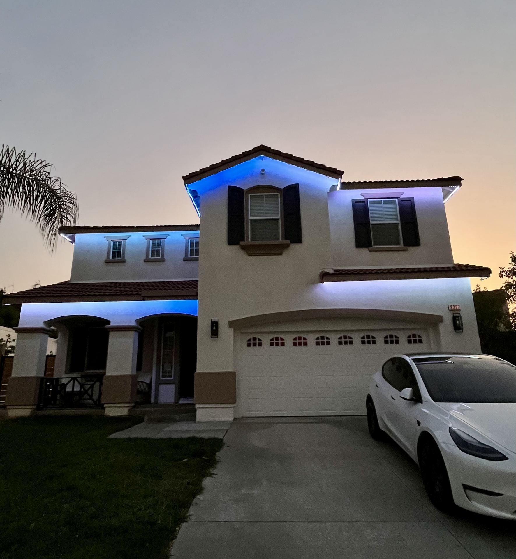 Two-story home with blue permanent lighting at dusk, Tesla in driveway