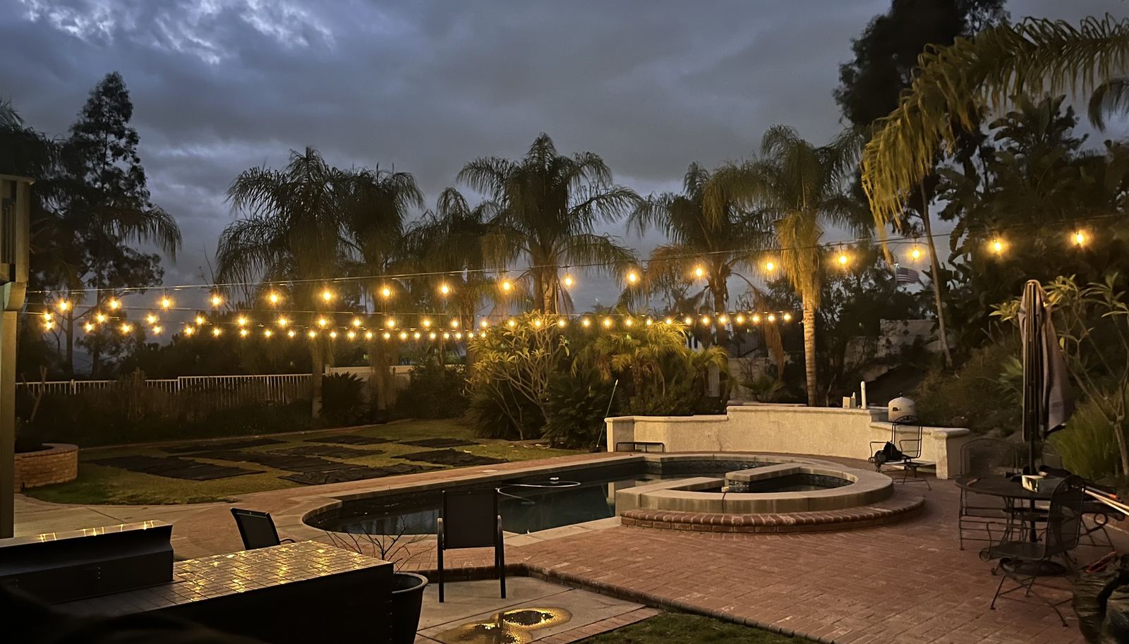 String lighting over backyard pool and firepit at dusk