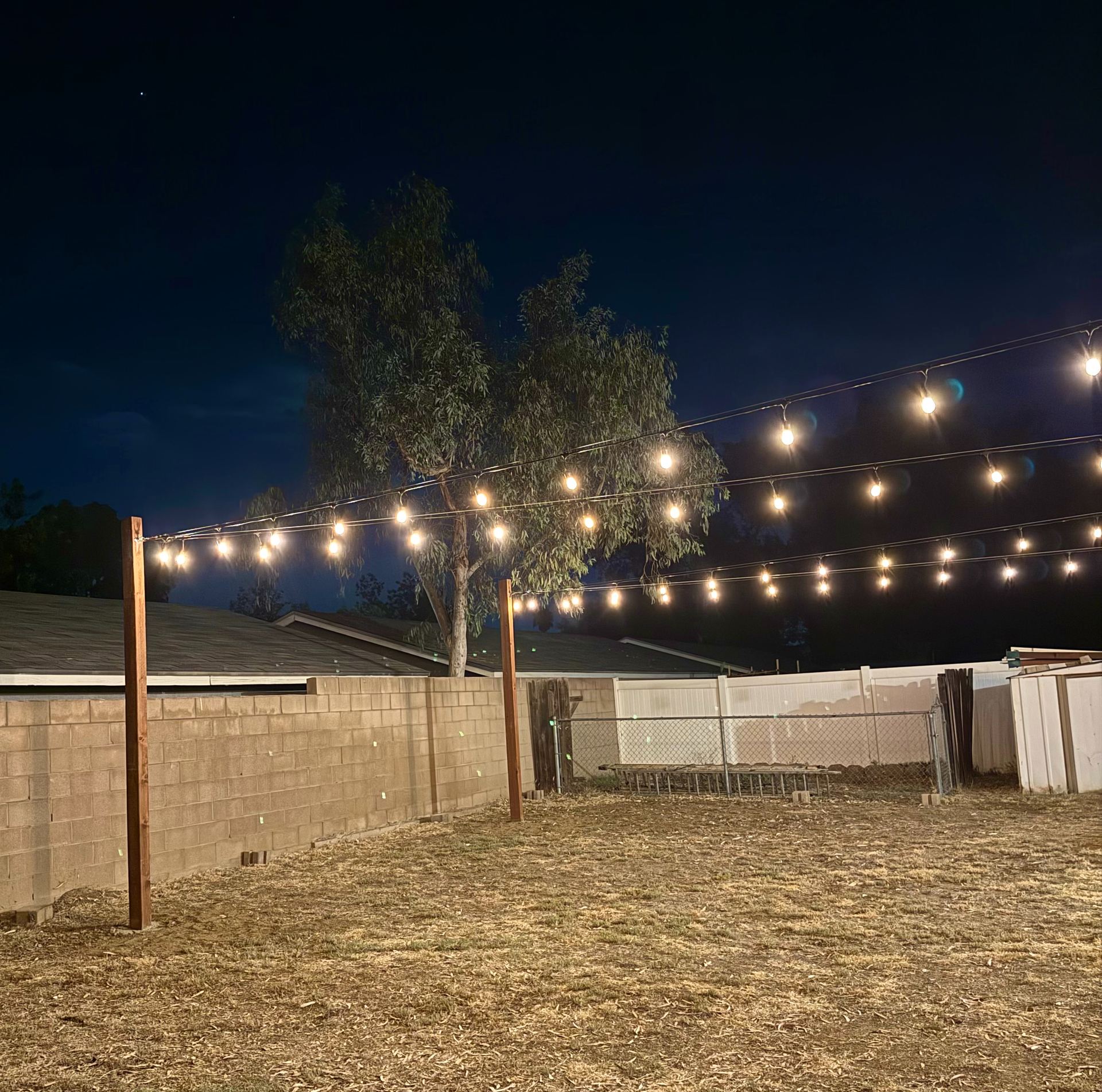 String lighting over open yard near pool seating area — bistro & string lighting install in Riverside, CA