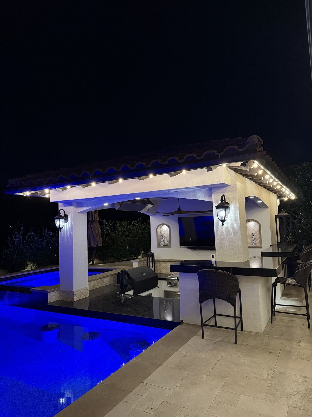 Outdoor kitchen blue pool night — bistro & string lighting install in Riverside, CA