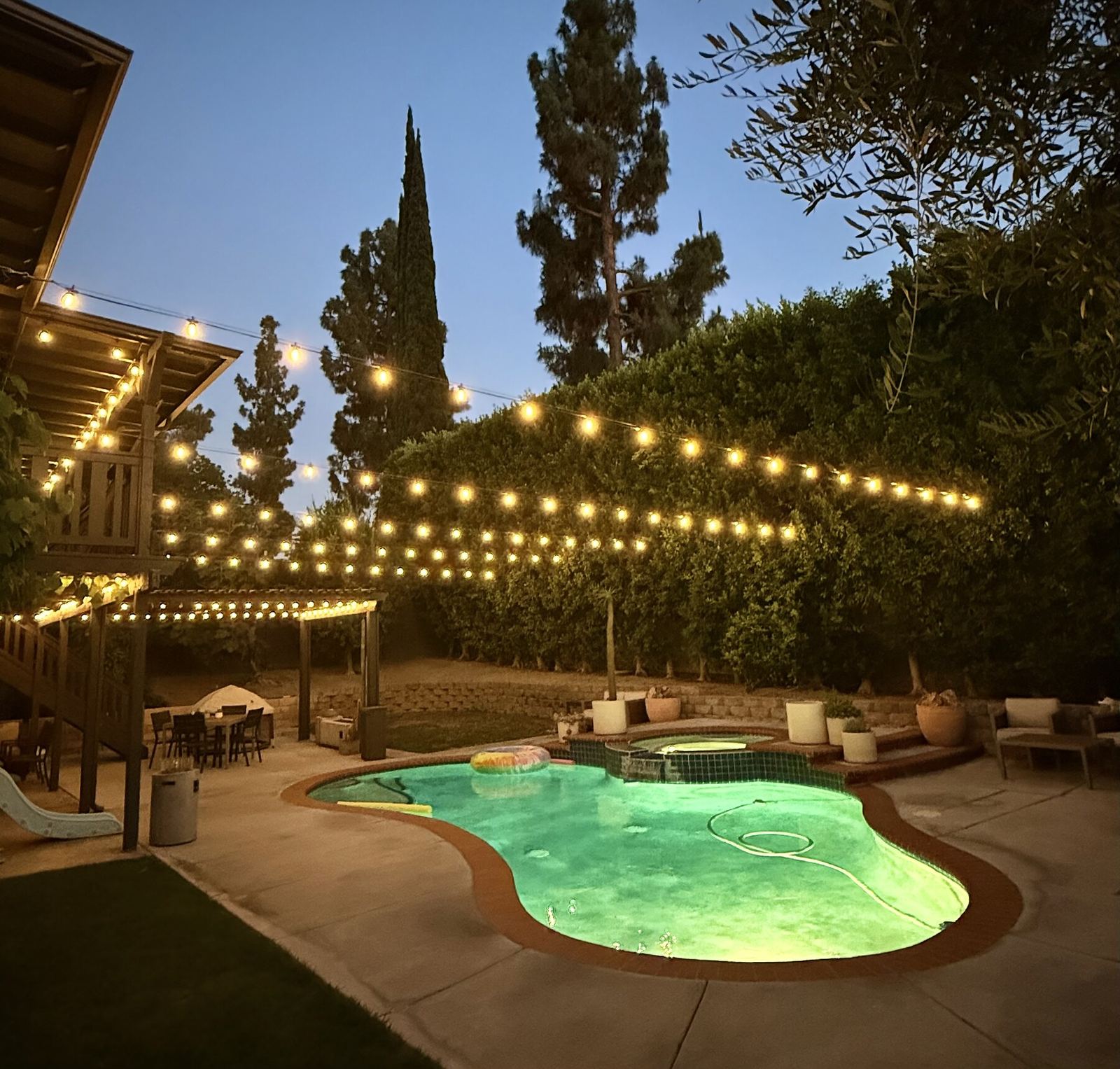 Pool green lit slide dusk — bistro & string lighting install in Riverside, CA